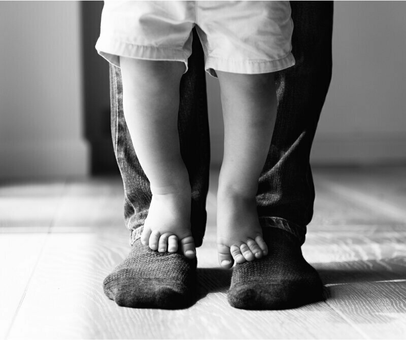 child standing on adult's feet