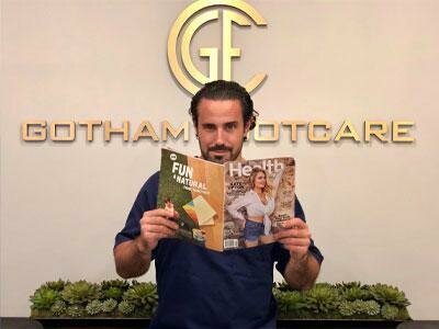 manhattan podiatrist dr. gotham reading a magazine in front of the gotham footcare wall logo